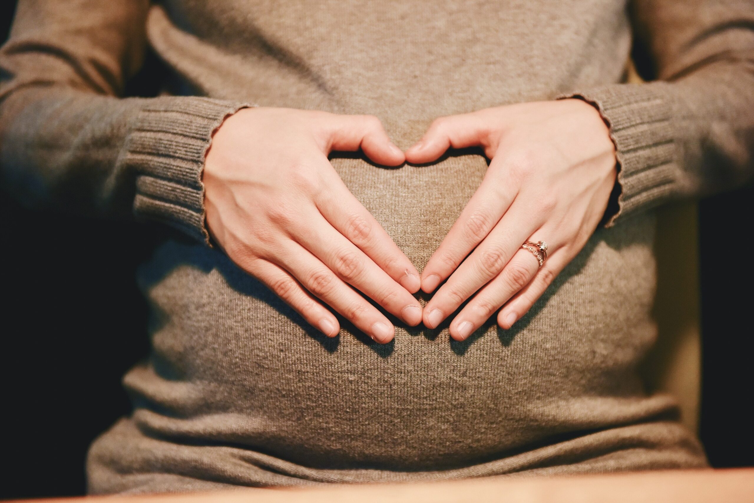 mulher grávida faz o símbolo de coração com as mãos na barriga