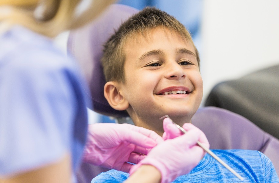 criança sentada sorri na cadeira de um consultório odontológico