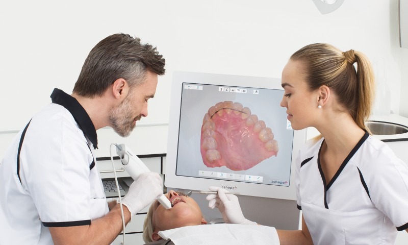 dois dentistas fazem escaneamento intraoral em uma paciente